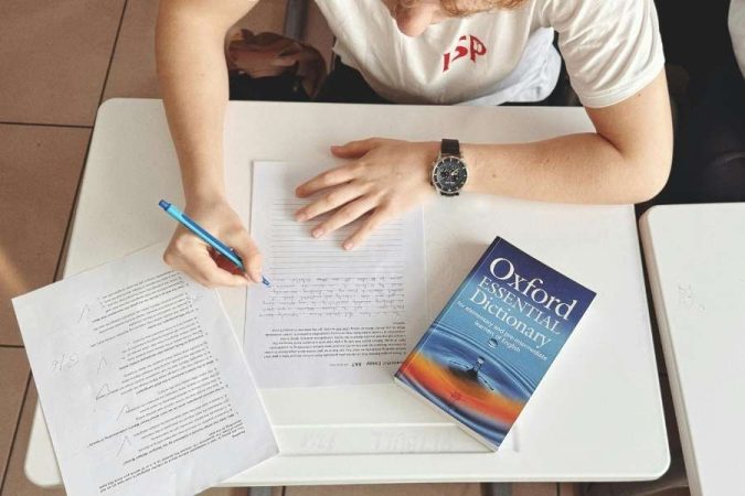 Un étudiant concentré écrit sur des feuilles lignées, avec un dictionnaire Oxford Essential à portée de main pour maîtriser les bases d'une langue.