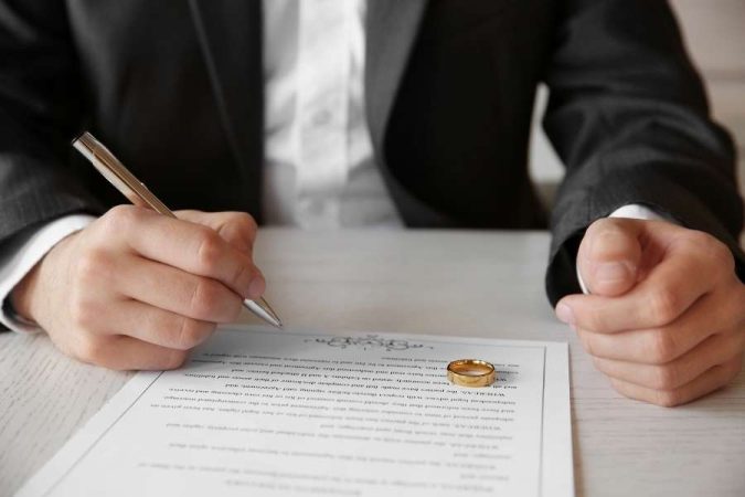 Un homme en costume s'apprête à signer un document de mariage civil, posant sa main sur l'alliance en or.