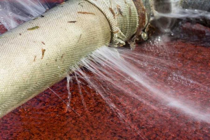 Un tuyau d'arrosage en tissu endommagé laissant échapper des jets d'eau à haute pression.
