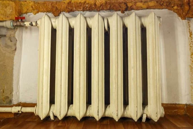 Un vieux radiateurs en fonte blanc installé contre un mur ancien.