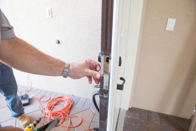 Un technicien installe une nouvelle serrure sur la tranche d'une porte d'entrée blanche, illustrant parfaitement l'action de sécuriser une porte de service.